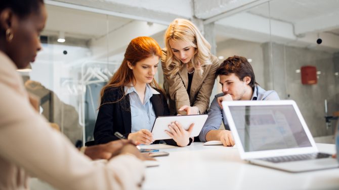 A team of three coworkers is discussing a practice using a tablet computer.