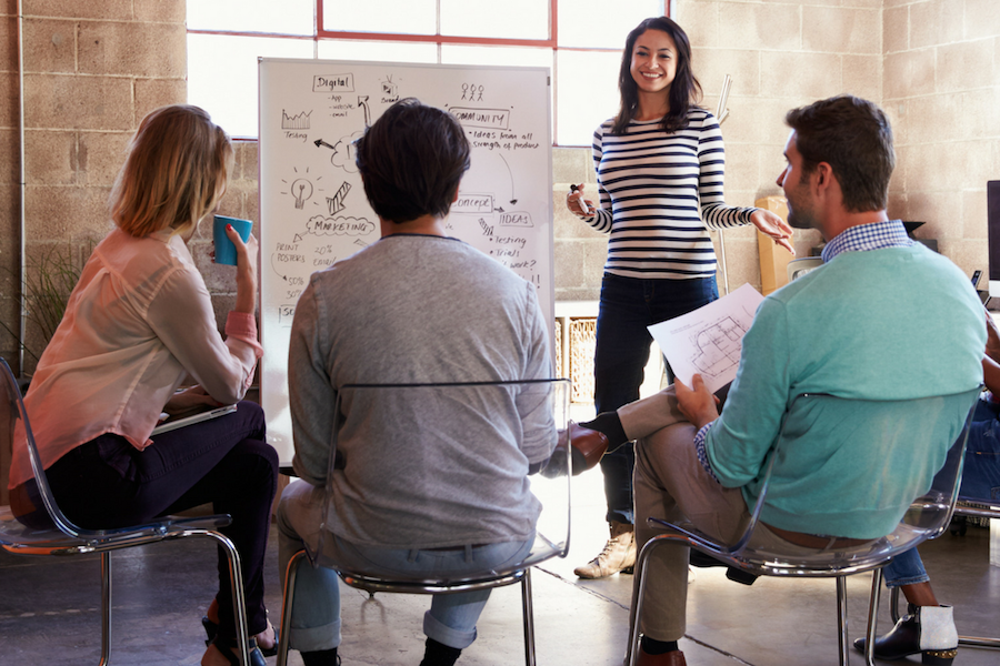 A team is holding a meeting in front of a white board.