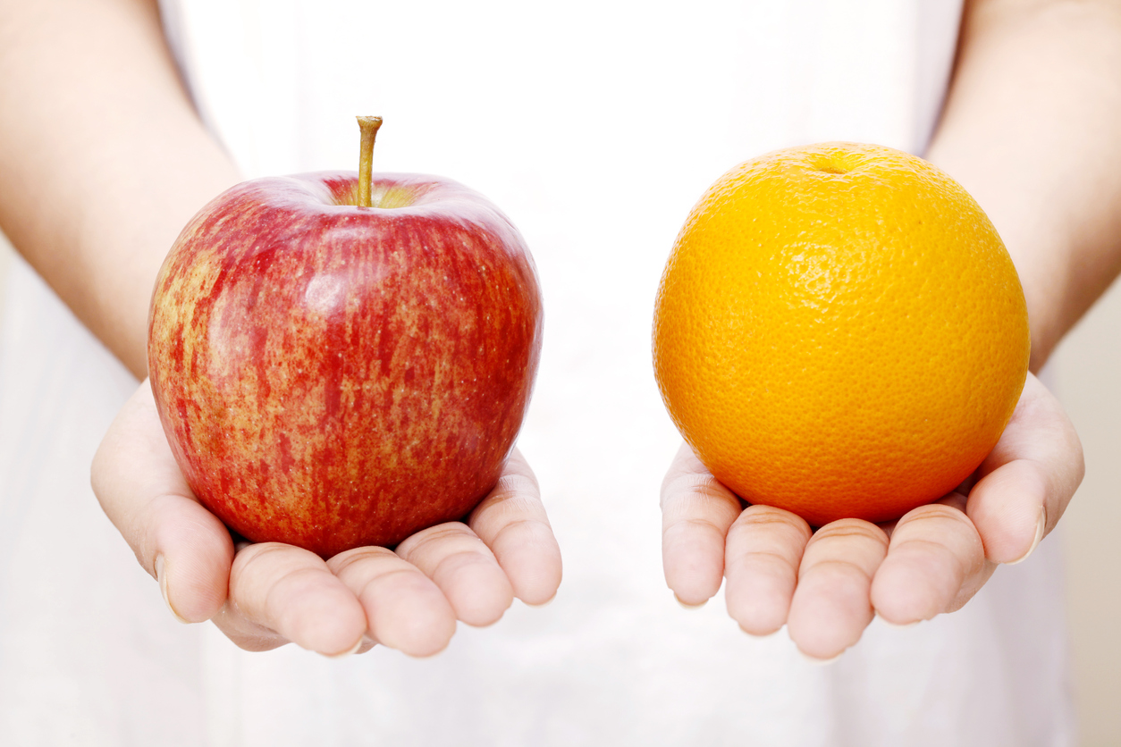 Two hands holding a red apple and an orange, respectively.