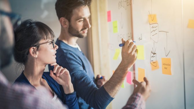 Male and female colleagues work on ideas using a whiteboard.