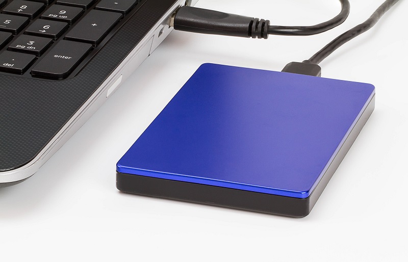 A blue mobile hard drive on a table is plugged into the laptop next to it.