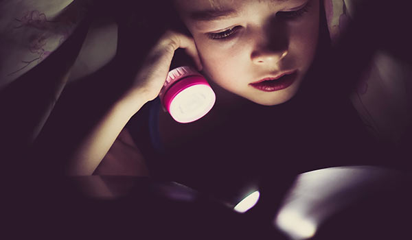 A young child reading a story using a flashlight.