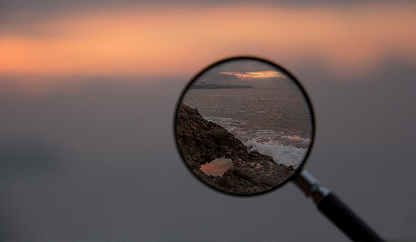 A magnifying glass in focus on mountains and the sea.