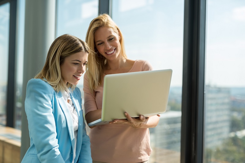 Two young women coworkers look at a laptop.