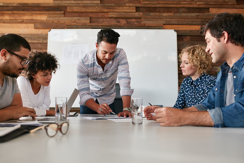 A group of team members watch their boss draw a demonstration.