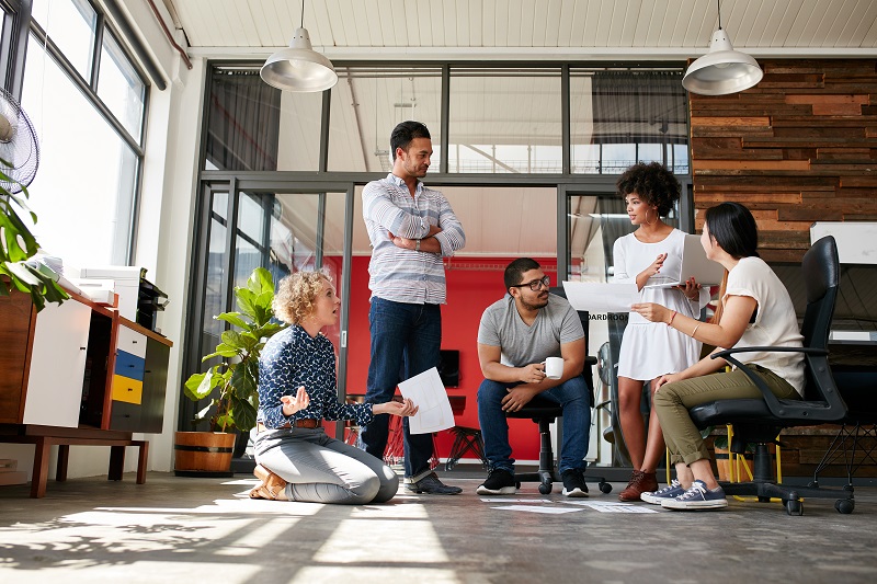 Five team members discuss statistics printed out onto paper.