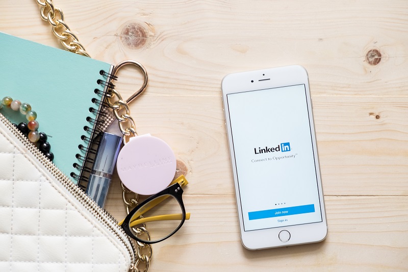 A picture of a desk with a mobile phone showing the Linkedin page.