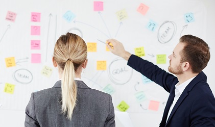 Two workers look at a whiteboard with notes on it.