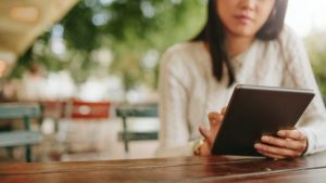Eine Frau sitzt an einem Tisch und informiert sich mit ihrem Tablet über Brand Manager.