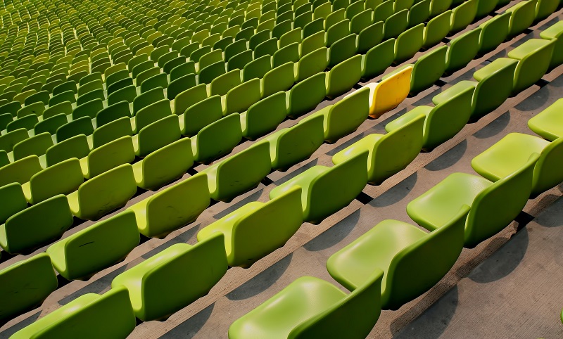 Green seats in a stadium with one yellow.