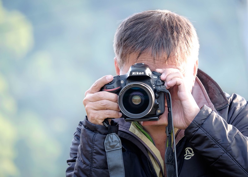 A man takes a photo using a Nikon camera.