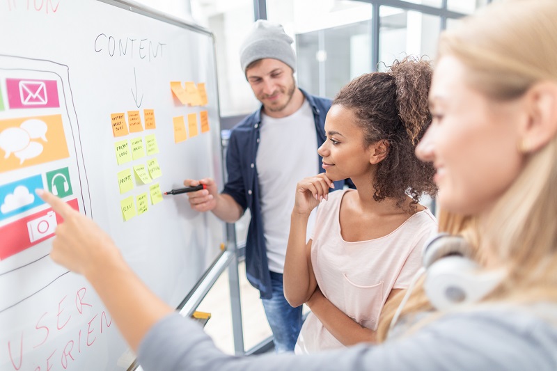 A group of workers study a whiteboard.