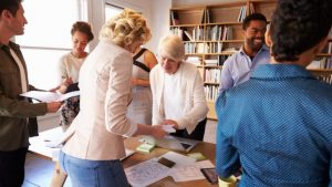 Eine Gruppe von Menschen steht um einen Tisch herum, der mit Papieren bedeckt ist und spricht über das Thema Markenstrategie.