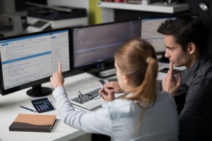 Zwei Mitarbeiter in einem Büro diskutieren über den Code einer Webseite, der auf einem Computerbildschirm vor ihnen angezeigt wird.