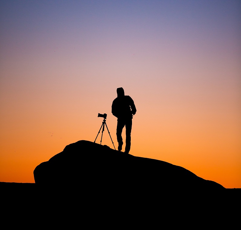 A cameraperson stands on a cliff.