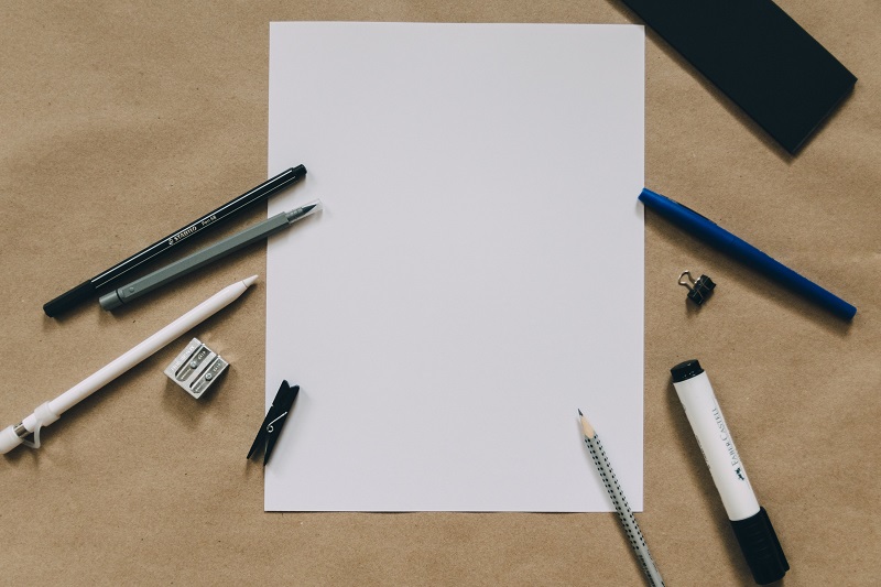 A blank sheet of paper surrounded by writing utencils.