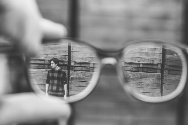 A pair of glasses viewing a man against a wall.