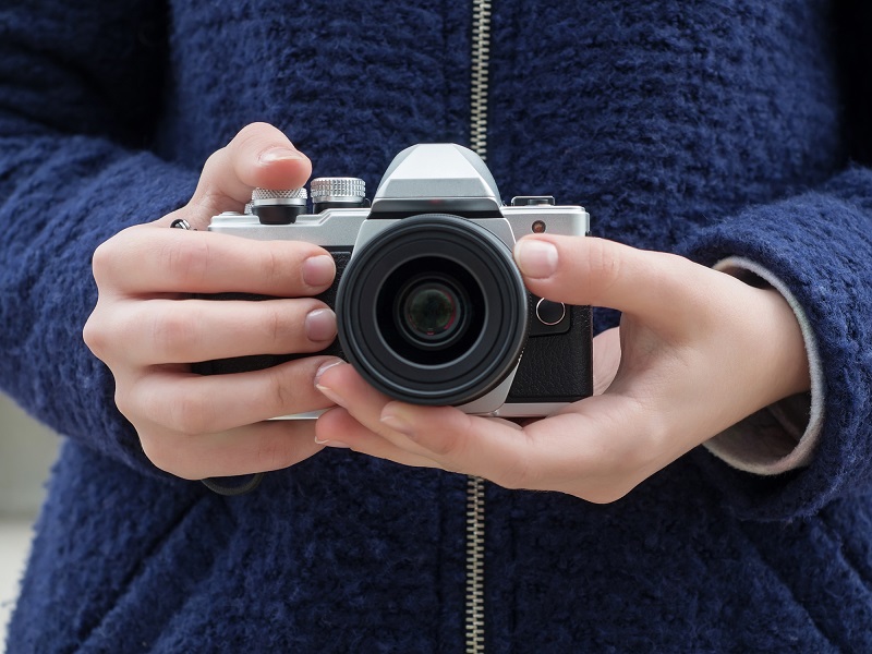 A woman holds a vintage Olympus camera.