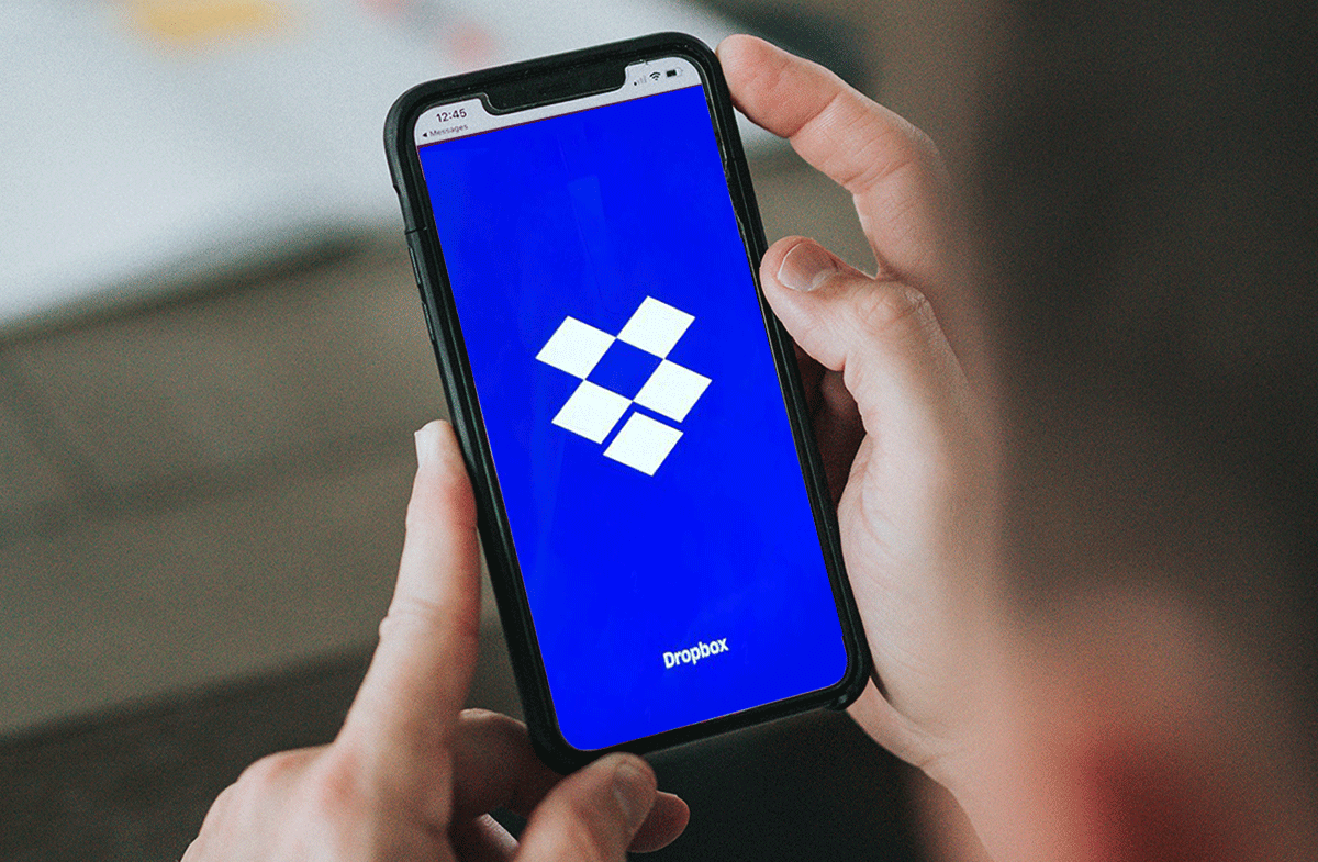 A person holding a smartphone that has Dropbox on it.