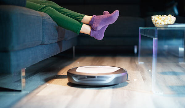 A person lifting their feet above a robot vacuum.