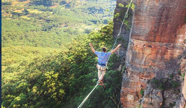 A man walking a tightrope over a steep cliff.