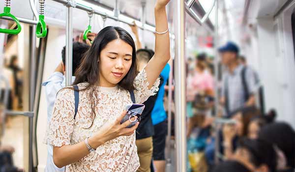 Young woman standing in a crowded subway car, reading something on her phone.