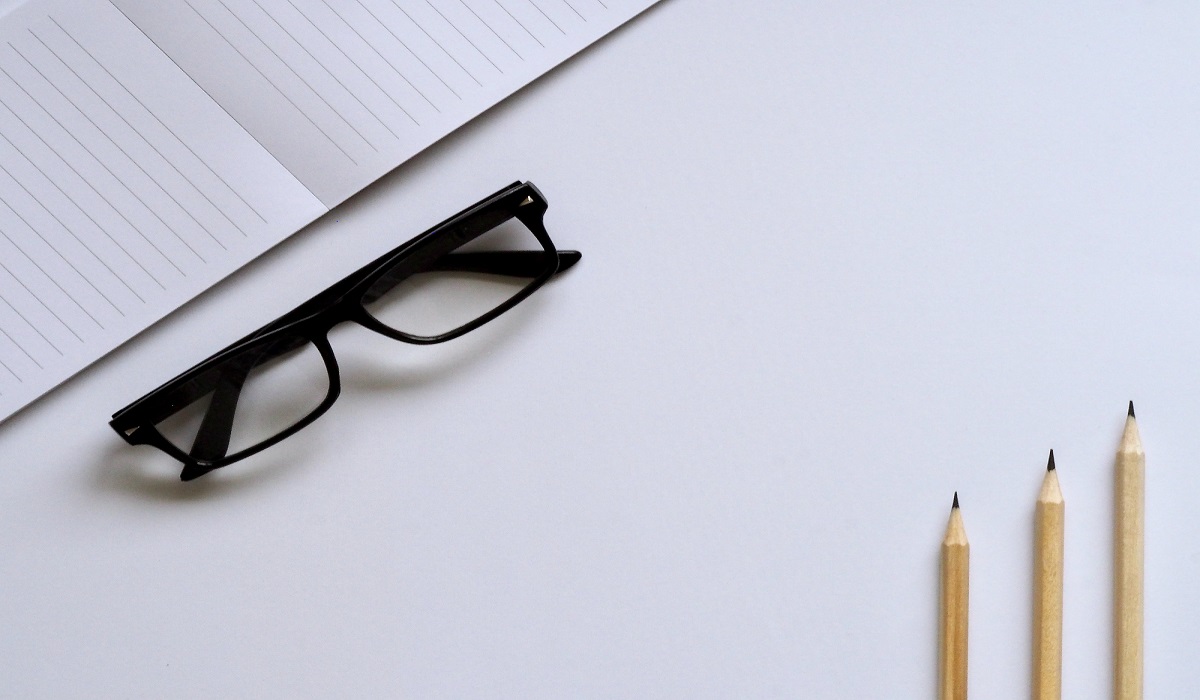 Glasses next to a notebook and pencils.