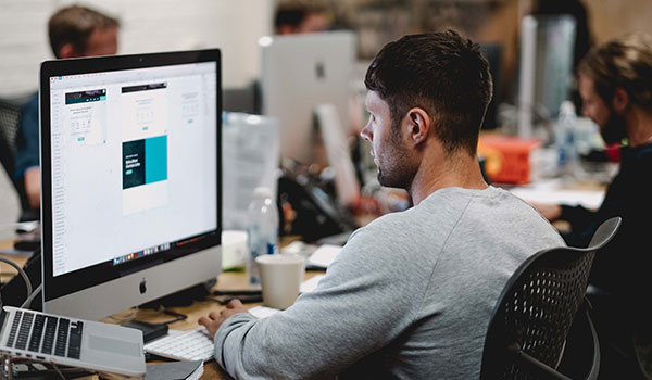 Man sitting at a computer in an office designing an email.