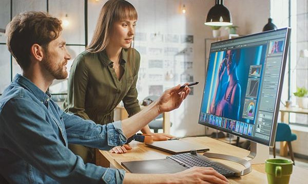 Two graphic designers point at computer monitor displaying a design layout.