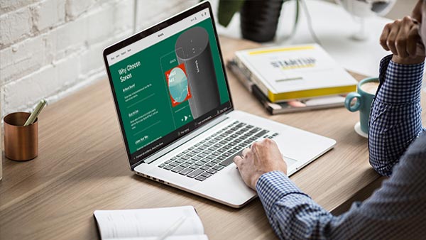 Man in checkered shirt at a desk viewing Sonos's website on a laptop computer.