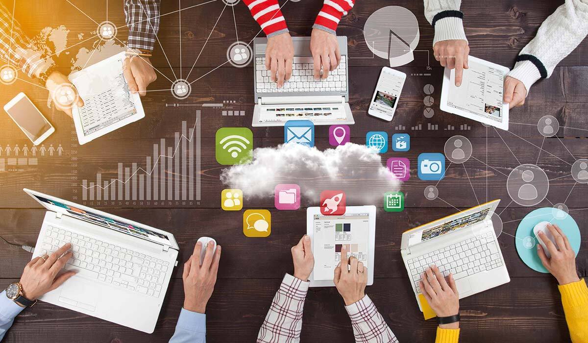 Overhead shot of a team with laptops around a conference table with icons representing content on the cloud.