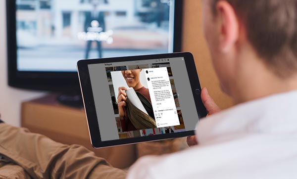 Man on a sofa viewing a branded Instagram post on his iPad while a TV ad plays in the background.